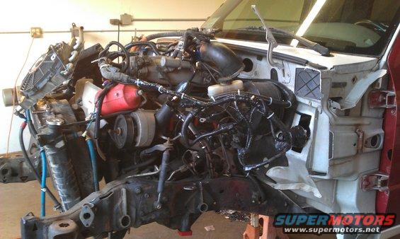 Truck engine bay with exposed engine, radiator, and wiring. Red fluid reservoir visible