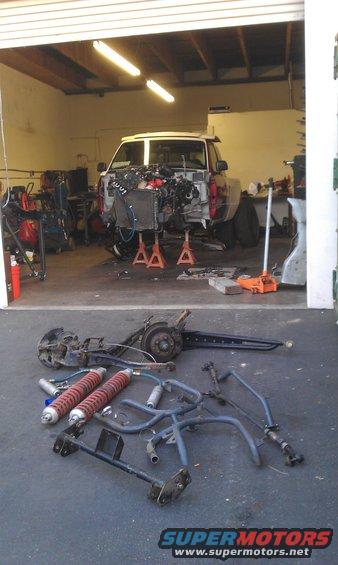 Truck in garage with engine removed, suspension parts on ground