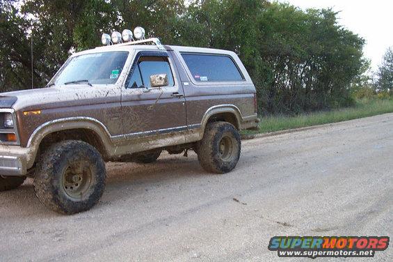Mud-covered 1980s Ford Bronco with roof-mounted lights on a dirt road