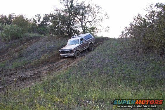 Ford Bronco climbing a muddy hill off-road. It has a two-tone paint job and roof lights