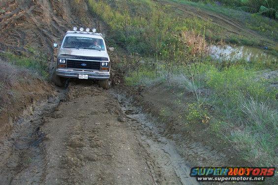 1982 Ford Bronco driving through a muddy track with lights on the roof