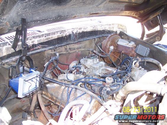 engine bay with carburetor, brake booster, and wiring. A work light is attached