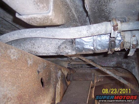 Undercarriage view of a vehicle's fuel line repaired with foil tape and hose clamps