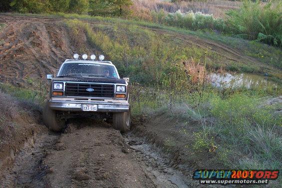 Ford Bronco driving through a muddy trail with lights on the roof
