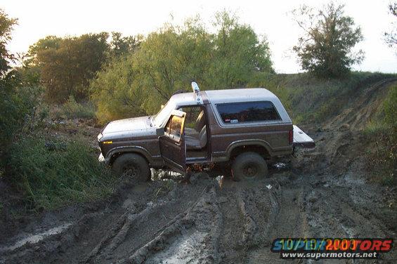 Brown and white Ford Bronco with doors open, stuck in thick mud on a dirt track