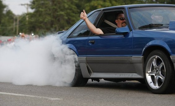 Blue 1990 Ford Mustang doing a burnout, driver giving a thumbs up
