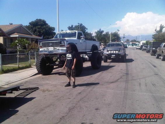 White lifted pickup truck with large tires, front view. A person stands nearby