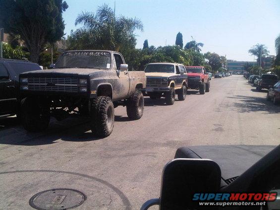 Line of lifted trucks and SUVs, including a Chevrolet pickup and Ford Bronco