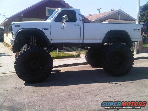 White pickup truck with massive tires and lift kit, parked on a street
