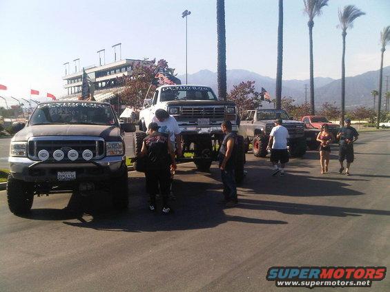 Several lifted trucks and SUVs parked in a lot with a grandstand in the background