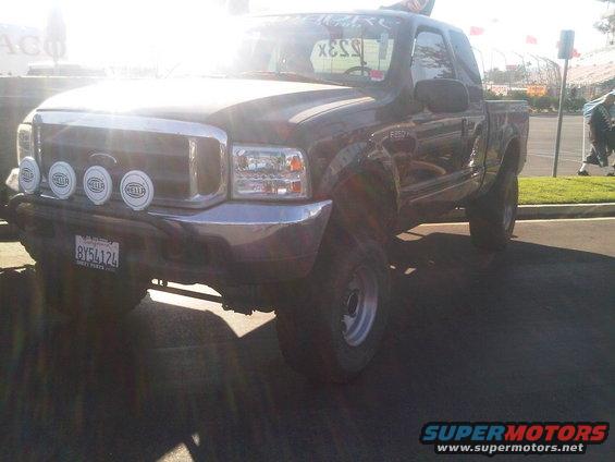Dark pickup truck with chrome grille and four Hella lights, lifted suspension, and aftermarket wheels
