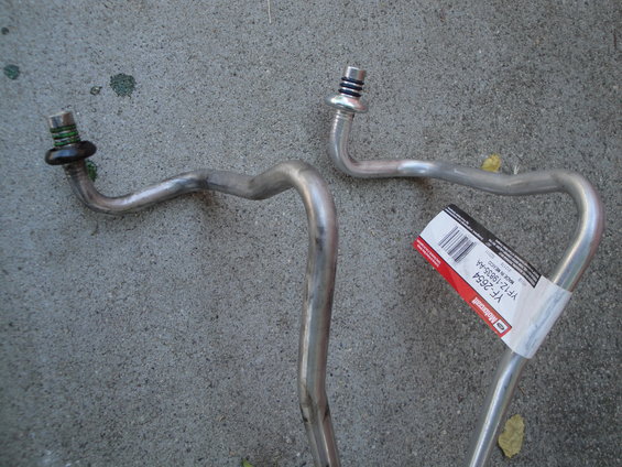 Two metal AC lines with fittings, one has a Ford Motorcraft label with part number YF1Z-19B35-AA