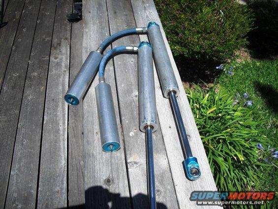 four shock absorbers with blue accents and hoses laid out on wooden planks