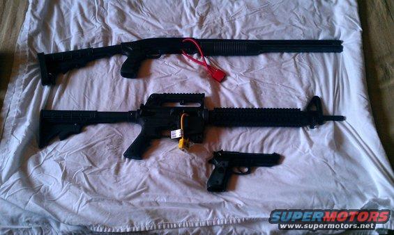 Shotgun, assault rifle, and pistol laid out on a white sheet