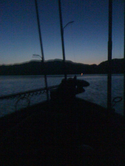 View from a boat deck looking out at water and hills at dusk