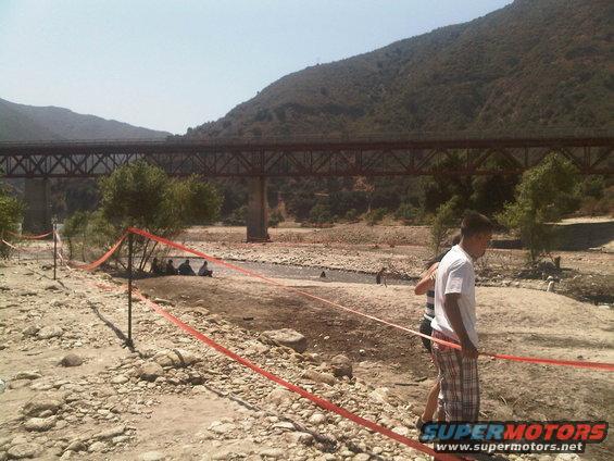 Dry riverbed with a bridge and people near orange caution tape