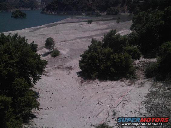 Dry lake bed with trees and water in background. Supermotors.net logo in corner