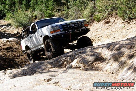 White 1995 Ford Bronco climbing rocks, lifted with off-road tires