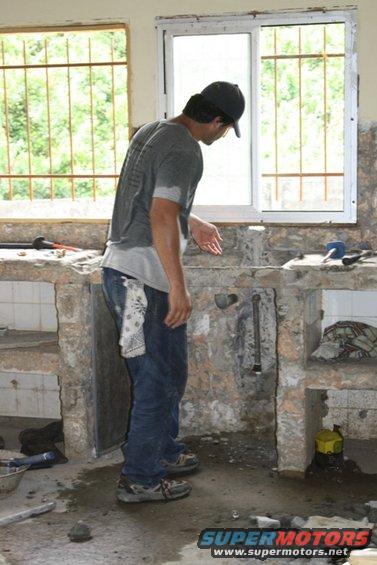 Man in baseball cap and jeans working on a sink demolition, with tools and debris around