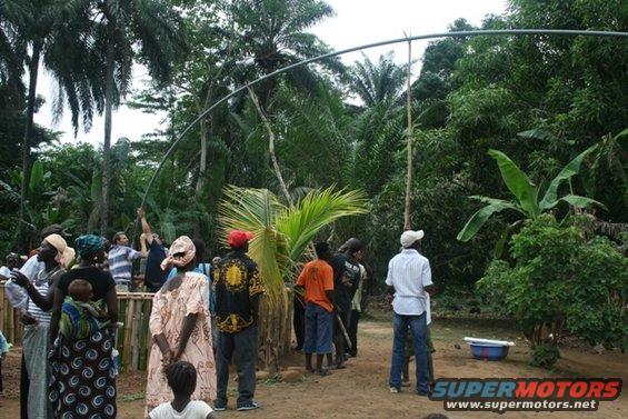 People gathered in a clearing with trees and a curved metal pole overhead