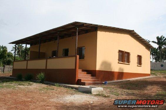 building with tan walls, brown trim, and a corrugated metal roof with a covered porch