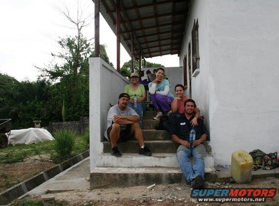 Group of five people sitting on concrete steps outside a white building with a covered porch