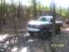 1989 Ford Bronco - A lifted Ford pickup truck navigates a muddy trail in a wooded area, with another vehicle in the distance.