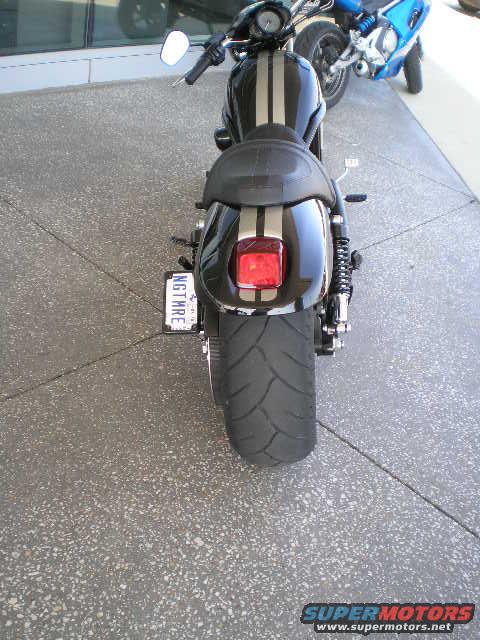 Black motorcycle with silver stripes, rear view. Another blue motorcycle is visible
