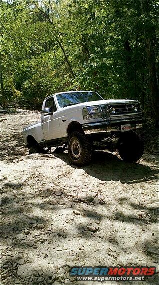1995 Ford F-150 lifted and off-roading on a dirt path with trees in the background