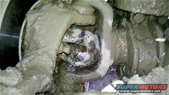 Mud-caked suspension part, possibly from a truck, with visible metal and some blueish material
