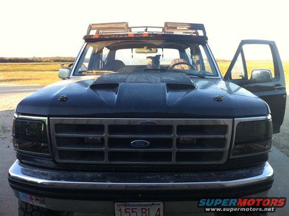 Dark blue Ford truck front view, hood scoop, roof rack with lights, driver's door open