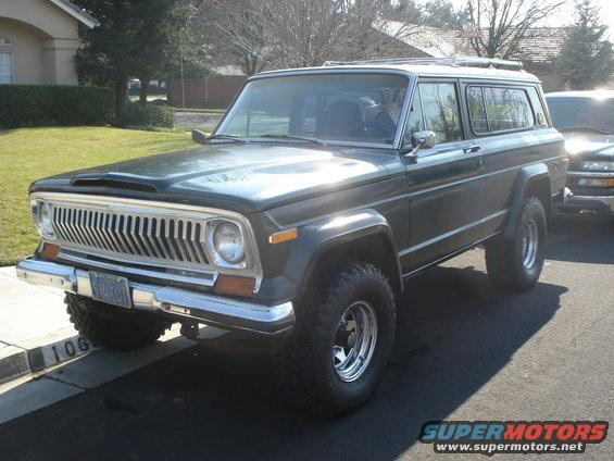Dark green Jeep Cherokee with chrome grille and aftermarket wheels, parked on a residential street