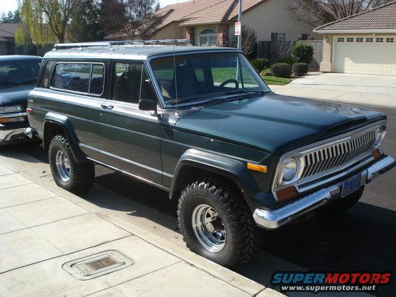 Dark green 1974 Jeep Cherokee 3-door with chrome grille and roof rack parked curbside