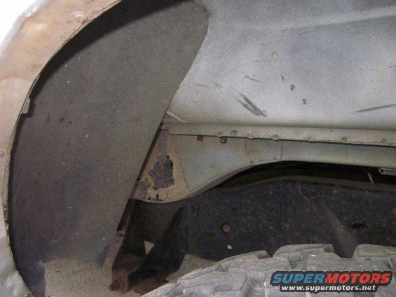 close-up of a vehicle's rear wheel well and frame showing rust and wear. A tire is visible at the bottom right