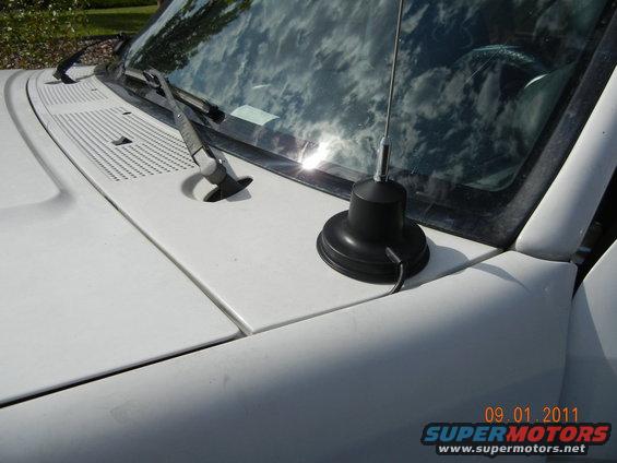 CB radio antenna mounted on the hood of a white vehicle, with windshield wipers visible