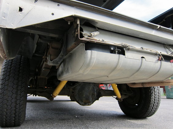 Underside view of a truck showing the fuel tank, leaf springs, differential, and yellow shock absorbers
