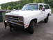 1987 Dodge 1500 - A white SUV is parked on asphalt with trees and dumpsters in the background.