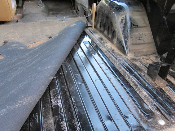 Interior of a vehicle with the floor mat peeled back, showing ribbed metal flooring