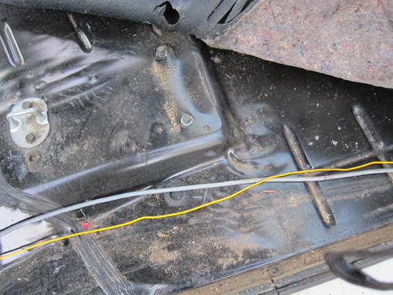 Interior floor of a vehicle showing dirt, wiring, and part of a seatbelt buckle