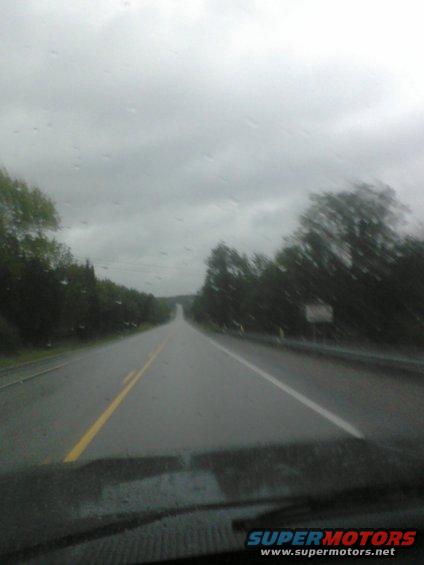 View from inside a vehicle looking out at a wet road under a cloudy sky