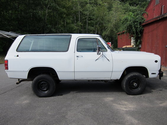 White SUV with black wheels parked on asphalt, side view. Some rust visible on lower body panels
