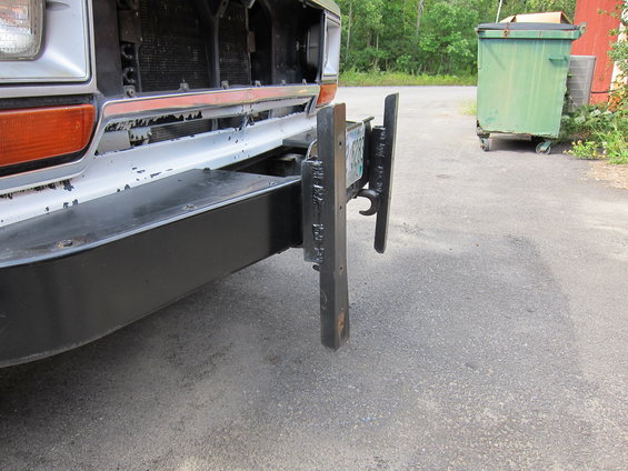 Truck front bumper with a black metal license plate mount attached. The bumper is white with peeling paint