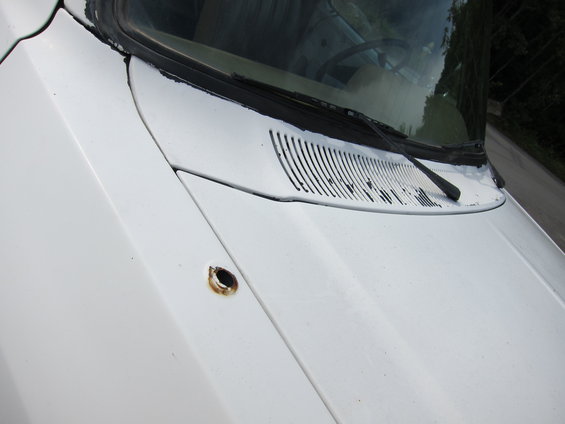White truck hood with a rusty hole near the windshield cowl