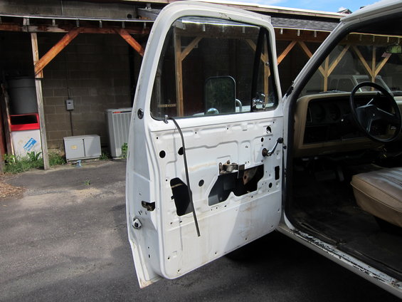 White truck door open, showing interior panel removed. Tan seat and dashboard visible