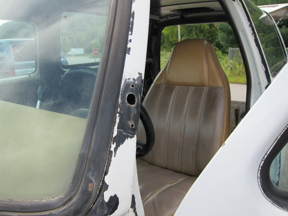White truck interior with tan seats, peeling paint on door frame, and steering wheel visible
