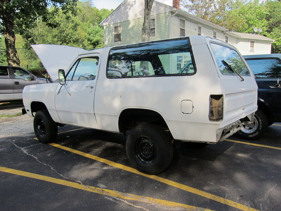 White SUV, possibly a Dodge Ramcharger, parked outdoors with hood up and rear bumper missing