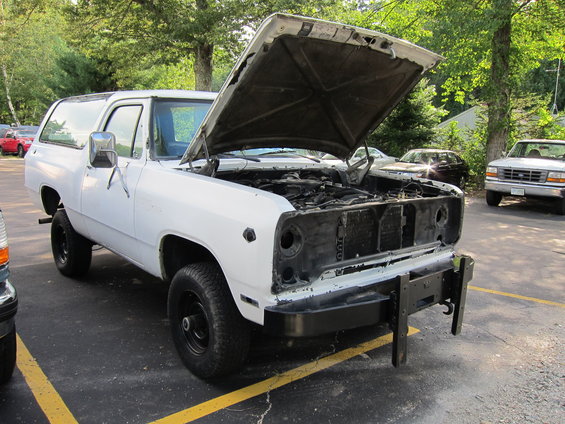 White SUV with hood open, missing grille, parked on asphalt with yellow lines