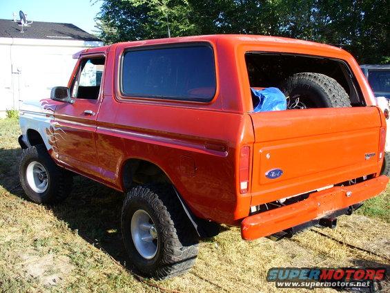 Orange Ford Bronco with white front fender and flame decals, lifted with large tires, seen from rear three-quarter angle