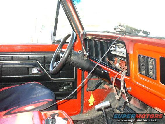 Interior of a red vehicle, showing the dashboard, steering wheel, and door panel. Wires are exposed near the radio