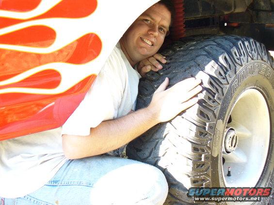 Man hugging large tire with flame decals on vehicle body